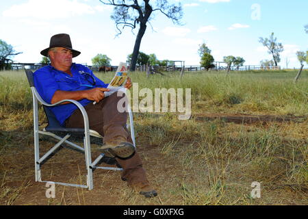 Un agriculteur d'âge moyen lit le journal à l'ombre d'un arbre sur une ferme près de Eidsvold, Queensland. Banque D'Images