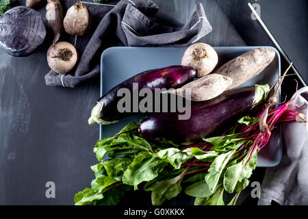 Les betteraves rouges, les aubergines et les feuilles de betterave sur la plaque avec l'ordinateur portable de recette sur le côté, vue de dessus Banque D'Images