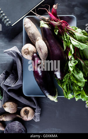 Betterave, aubergines et de feuilles de betterave sur la plaque avec l'ordinateur portable noir sur le côté, vue de dessus Banque D'Images