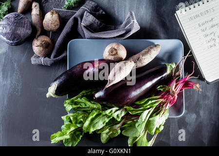 Les betteraves rouges, les aubergines et les feuilles de betterave sur la plaque avec des recettes sur le côté de l'ordinateur portable, vue du dessus Banque D'Images