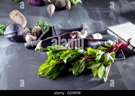 Les betteraves rouges, les aubergines et les feuilles de betterave sur la plaque avec un chiffon et de l'ordinateur portable noir sur le côté Banque D'Images