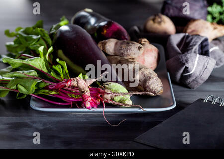 Les betteraves rouges, les aubergines et les feuilles de betterave sur la plaque avec l'ordinateur portable noir sur le côté Banque D'Images