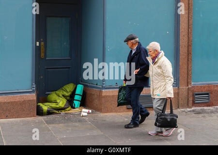 L'homme et de la femme en passant devant quelqu'un sans-abri dans un magasin porte, Glasgow, ville, Ecosse, Royaume-Uni Banque D'Images