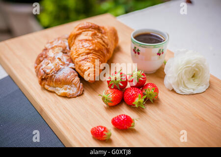 Français doux croissant et baies, tasse de café et de fleurs fraîches. Focus sélectif. Banque D'Images