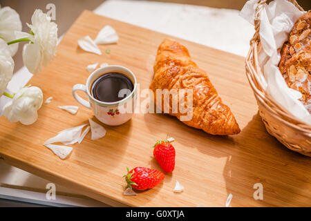 Français doux croissant et baies, tasse de café et de fleurs fraîches. Focus sélectif. Banque D'Images