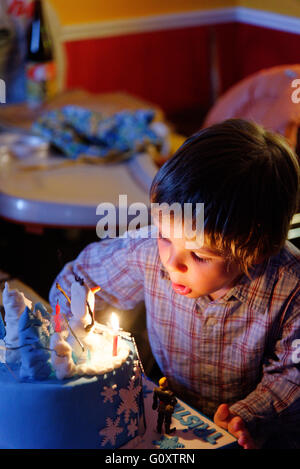 Un jeune garçon (4 ans) blowing out candles sur son gâteau d'anniversaire Banque D'Images