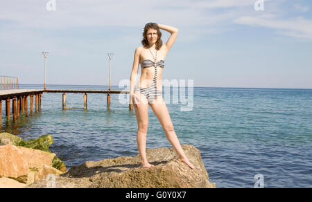 Jeune européen woman in bikini se dresse sur grosse pierre sur mer plage. Banque D'Images