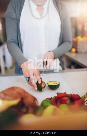 Cropped shot of woman cutting fruits Avocat au compteur. Femme travaillant au bar à jus. Banque D'Images