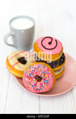 Tasse de lait chaud et assiette de beignets avec glaçage multicolore Banque D'Images