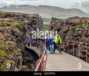 Sud-ouest de l'Islande, Islande. 4 Août, 2015. Les touristes à pied sur un pont sentier entre des murs de roche volcanique par Almannagja célèbre canyon dans le Parc National de Thingvellir, d'un marquage de la vallée du Rift, la crête de la dorsale médio-atlantique entre les plaques eurasienne et nord-américaine, il s'agit d'une représentation visuelle de la dérive formé entre deux plaques tectoniques. C'est l'une des attractions touristiques les plus visitées en Islande où le tourisme est devenu un secteur en pleine croissance de l'économie.Les touristes à pied sur un pont sentier entre des murs de roche volcanique à travers célèbre Almannagja en canyon National Thingvellir Banque D'Images