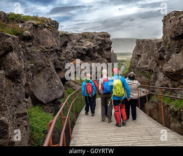 Sud-ouest de l'Islande, Islande. 4 Août, 2015. Les touristes à pied sur un pont sentier entre des murs de roche volcanique par Almannagja célèbre canyon dans le Parc National de Thingvellir, d'un marquage de la vallée du Rift, la crête de la dorsale médio-atlantique entre les plaques eurasienne et nord-américaine, il s'agit d'une représentation visuelle de la dérive formé entre deux plaques tectoniques. C'est l'une des attractions touristiques les plus visitées en Islande où le tourisme est devenu un secteur en pleine croissance de l'économie.Les touristes à pied sur un pont sentier entre des murs de roche volcanique à travers célèbre Almannagja en canyon National Thingvellir Banque D'Images