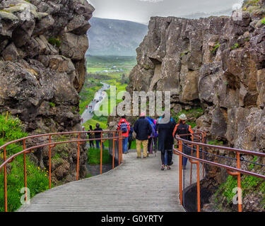 Sud-ouest de l'Islande, Islande. 4 Août, 2015. Les touristes à pied sur un pont sentier entre des murs de roche volcanique par Almannagja célèbre canyon dans le Parc National de Thingvellir, d'un marquage de la vallée du Rift, la crête de la dorsale médio-atlantique entre les plaques eurasienne et nord-américaine, il s'agit d'une représentation visuelle de la dérive formé entre deux plaques tectoniques. C'est l'une des attractions touristiques les plus visitées en Islande où le tourisme est devenu un secteur en pleine croissance de l'économie.Les touristes à pied sur un pont sentier entre des murs de roche volcanique à travers célèbre Almannagja en canyon National Thingvellir Banque D'Images
