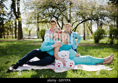 Happy pregnant couple avec deux fils hugging et assis sur fond plaid nature printemps Banque D'Images