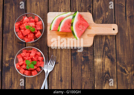 Melon coupé en petits cubes ou peaces dans deux plats en verre sur fond de bois- vue d'en haut. Banque D'Images