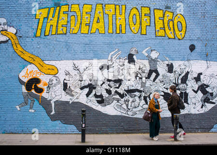 Hipster couple debout devant un mur avec un grand de l'écriture Graffiti 'la mort de l'ego" dessus. Banque D'Images