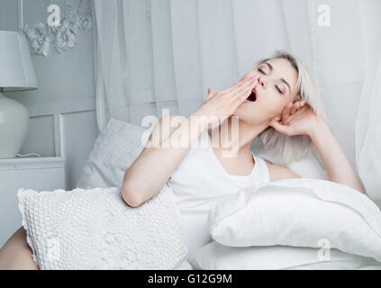 Belle jeune blonde woman yawning in bed at home Banque D'Images