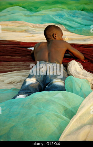 Jeune homme allongé sur le ventre sur les filets de pêche colorés mis à sécher sur la plage de Chembe, Cape Maclear, Malawi Banque D'Images