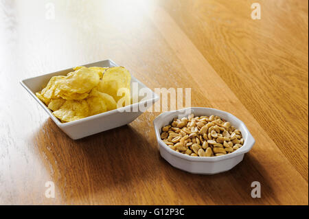 Bols de chips et les cacahuètes sur une table à manger en chêne. Banque D'Images
