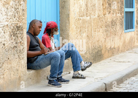 Un dessinateur de rue et un homme âgé avec un cigare, vous détendre sur une porte dans la Vieille Havane, La Havane, Cuba Banque D'Images