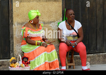 Un vendeur de poupées portant des costumes traditionnels et fumer un cigare se détend avec un compagnon dans la Vieille Havane, La Havane, Cuba Banque D'Images