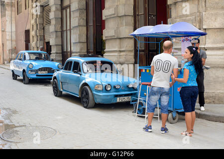 Un vendeur de glace parcs à côté de deux voitures classiques bleu dans la Vieille Havane, La Havane, Cuba Banque D'Images