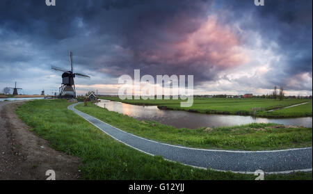 Beau paysage avec moulins à vent hollandais traditionnel près du fameux canaux d'eau avec ciel dramatique nuages colorés, et trail Banque D'Images