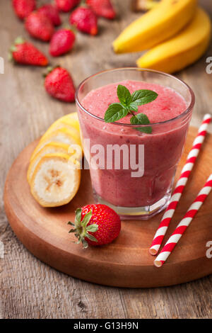 Smoothie à la banane et à la fraise dans le verre, fraises et bananes sur le vieux fond de bois Banque D'Images