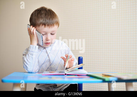 Petit garçon est assis à un bureau à l'école et de parler au téléphone Banque D'Images