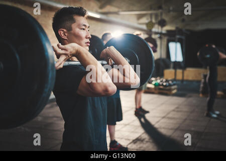 Mettre en place des barres de levage de jeune homme à l'accent, s'entraîner dans un gymnase avec d'autres personnes Banque D'Images