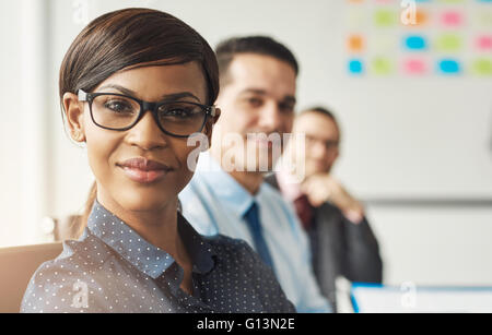 Beautiful smiling business woman wearing eyeglasses et blanc polka dotted shirt assis avec leurs collègues masculins au travail Banque D'Images