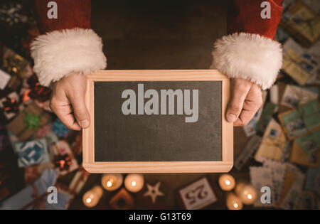 Santa Claus holding a blank blackboard mains close up, vue du dessus de bureau, avec des dons et des lettres de Noël sur fond de Banque D'Images