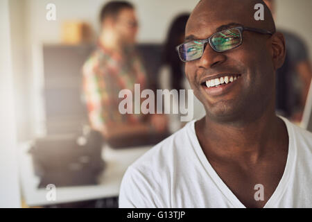 Close up of handsome smiling worker en chemise blanche et lunettes avec trois employés hors foyer derrière lui en séance Banque D'Images