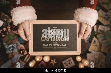 Père Noël tenant une ardoise sur Joyeux Noël et Bonne Année message, Desktop avec des dons et des lettres de Noël sur ba Banque D'Images