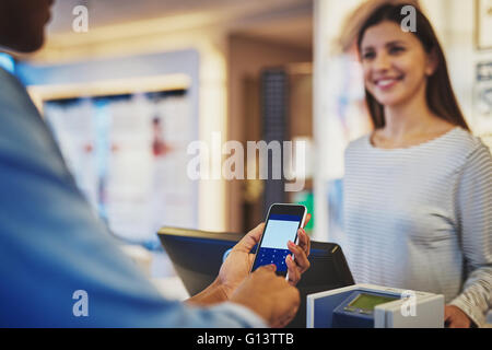 A proximité de la saisie d'informations sur le téléphone en tant que caissier femelle sourit dans store Banque D'Images