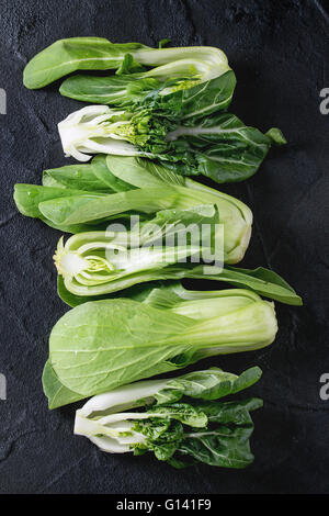 Assortiment de matières premières entières et tranchées petits bok choy (chou chinois) sur fond texturé noir. Top View with copy space Banque D'Images