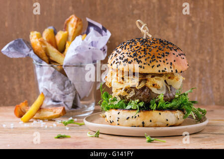 Hamburgers maison avec du boeuf, oignons frits et pousses de pois, servis sur une plaque en céramique avec des pommes de terre sautées en bois sur zone texturée Banque D'Images