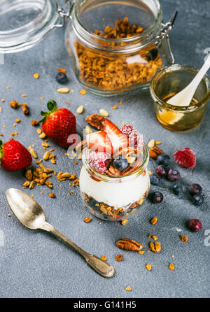 L'avoine yogourt avec granola de baies fraîches, les noix, le miel et les feuilles de menthe dans un bocal en verre sur fond texturé de béton gris, sélective fo Banque D'Images