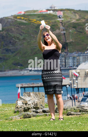 Aberystwyth, Pays de Galles, Royaume-Uni. 8 mai, 2016. Météo France : que les températures atteignent les 20 degrés Celsius dans certaines régions de la Grande-Bretagne, les gens peuvent profiter de la chaleur du soleil pour l'Aberystwyth, sur la côte ouest de la Baie de Cardigan au Pays de Galles. photo : Hayley Reeves (34) de Oswestry, sur une journée à la mer, prend une promenade avec les selfies et la ville en arrière-plan Crédit photo : Keith Morris / Alamy Live News Banque D'Images