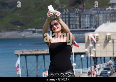 Aberystwyth, Pays de Galles, Royaume-Uni. 8 mai, 2016. Météo France : que les températures atteignent les 20 degrés Celsius dans certaines régions de la Grande-Bretagne, les gens peuvent profiter de la chaleur du soleil pour l'Aberystwyth, sur la côte ouest de la Baie de Cardigan au Pays de Galles. photo : Hayley Reeves (34) de Oswestry, sur une journée à la mer, prend une promenade avec les selfies et la ville en arrière-plan Crédit photo : Keith Morris / Alamy Live News Banque D'Images