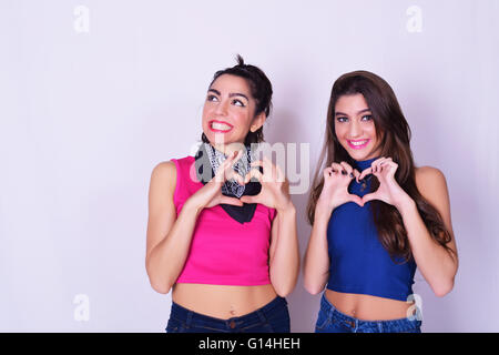 Portrait de deux belles faisant une forme de coeur avec les mains. Concept d'amitié. Amis mode et élégant, le dos gris plus isolés Banque D'Images