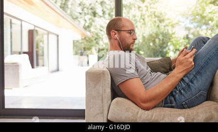 Vue côté droit d'un homme en utilisant sa tablette tout en étant assis sur le canapé à la maison. Caucasian man relaxing on couch using tablet pc. Banque D'Images