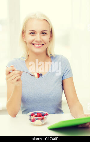 Smiling woman eating fruits avec tablet pc at home