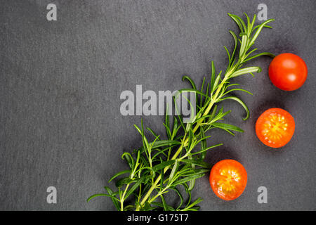 Brindille de romarin vert frais et tomates cerises sur fond d'ardoise gris foncé Banque D'Images