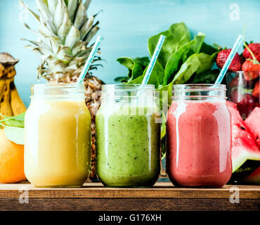 Smoothies aux fruits fraîchement mélangé de diverses couleurs et saveurs dans des bocaux en verre. Jaune, rouge, vert. Fond bleu turquoise Banque D'Images