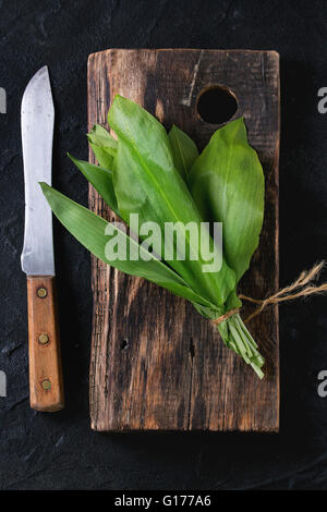 Bunch of fresh ramson sur planche à découper en bois avec couteau vintage sur fond texturé noir. Vue d'en haut Banque D'Images