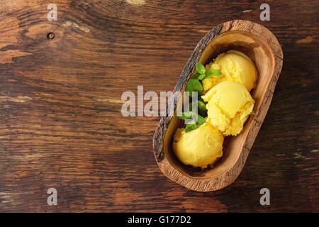 La crème glacée mangue fait maison avec de la menthe fraîche dans un bol en bois d'olive, servi sur fond texturé en bois. Top View with copy space Banque D'Images