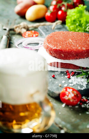 Burger de viande de boeuf haché cru escalopes steak avec des légumes et l'assaisonnement,bière sur planches de bois vintage Banque D'Images