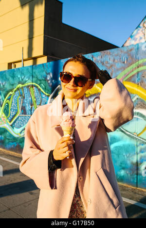 Portrait de jeune femme élégante eating ice cream cone en face de mur de graffiti, Venice Beach, California, USA Banque D'Images