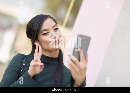 Femme faisant signe de la paix et de l'aide à prendre la moue smartphone selfies Banque D'Images