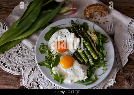 Asperges grillées au parmesan sur lit de salade de roquette et surmontée d'oeufs frits Banque D'Images